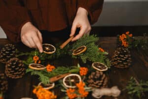 Alameda Post - a person makes a wreath out of natural materials including evergreen, pinecones, and dried oranges