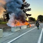 Alameda Post - an AFD firefighter sprays water on an encampment fire near Alameda Point