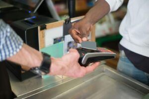 Alameda Post - a cashier holds out a card reader, and a customer taps their card