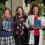 Alameda Post - a student and teacher stand holding plaques, and another woman stands in between them