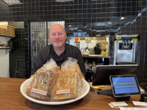 Alameda Post -John Thiel stands behind the counter of Pizzeria Pappo and smiles
