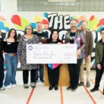 Alameda Post - a group of nine people are posing for the camera and holding a large check