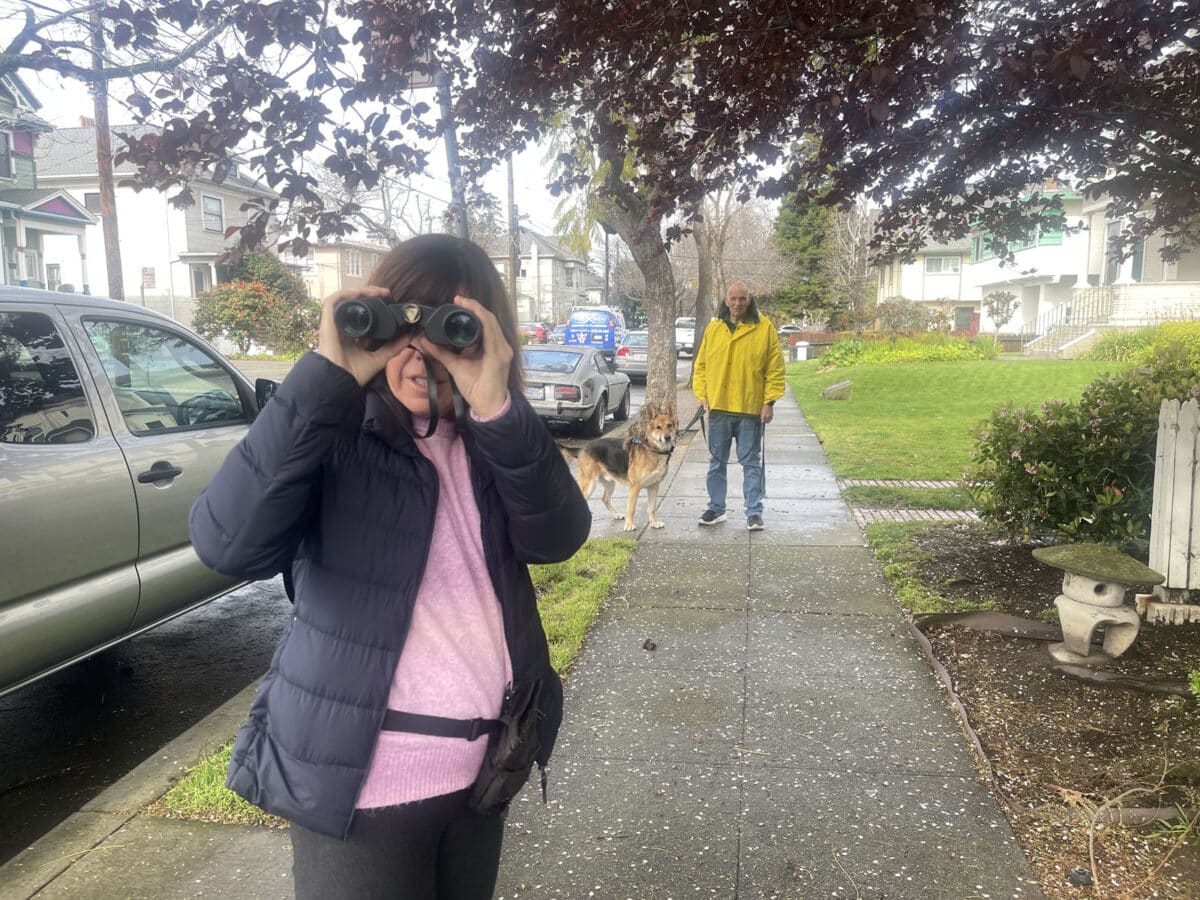 Alameda Post - a man walks Mouf, and a woman holds binoculars 