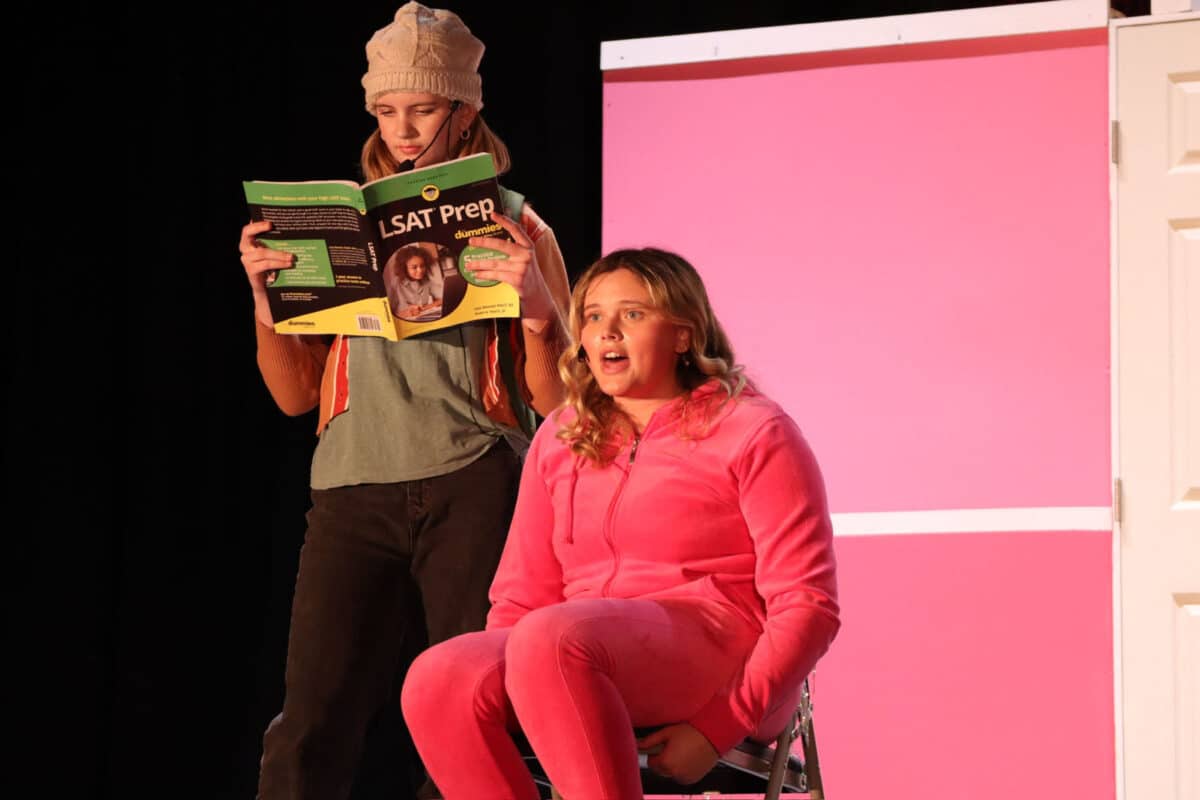 Alameda Post - an actress in a pink fuzzy track suit sits next to another actor holding an LSAT prep book