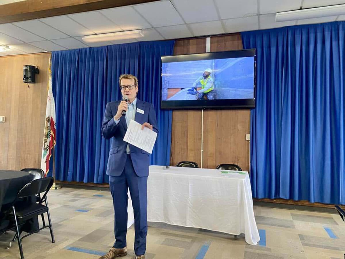 Alameda Post - Jim Oddie stands in front of a room and speaks into a microphone