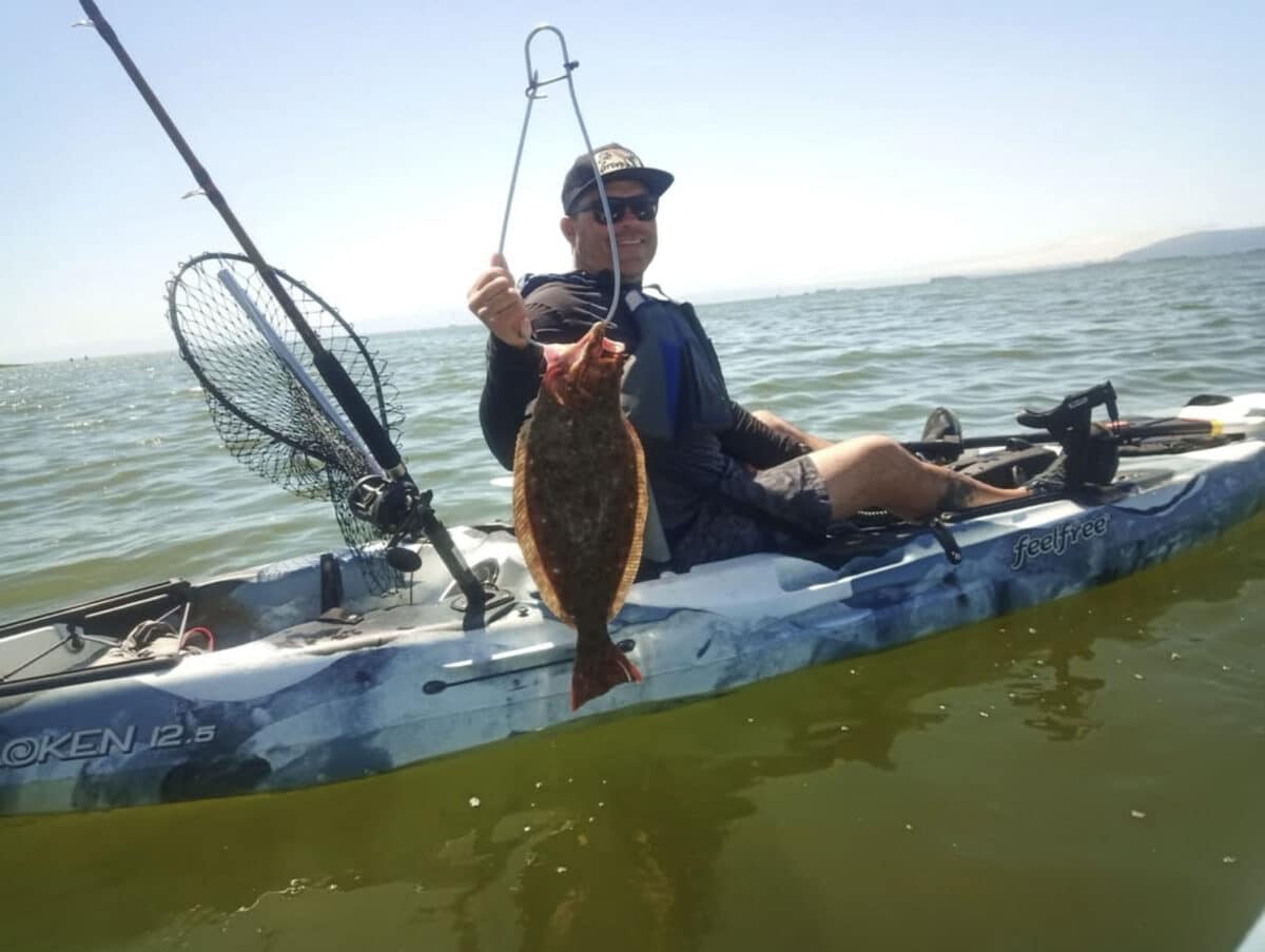 Alameda Post - a person on a kayak holds up a halibut next to fishing gear