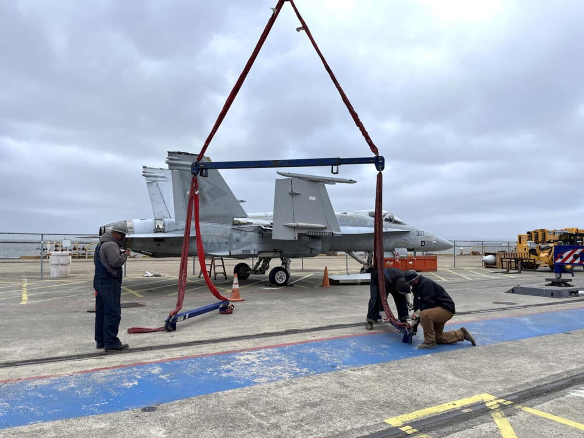 Alameda Post - workers secure straps to a F/A-18C Hornet retired fighter jet