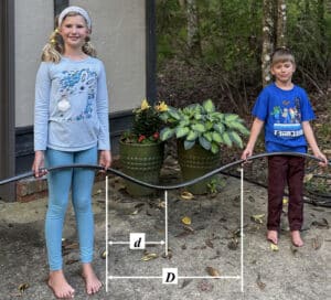 Alameda Post - Two kids hold a garden hose that sags and forms a shallow half circle between them. A Distance labeled capital D is marked between the kids' hands. Around halfway between the two kids' hands, the lowest point of the curve is labeled lowercase d distance from one child's hand.