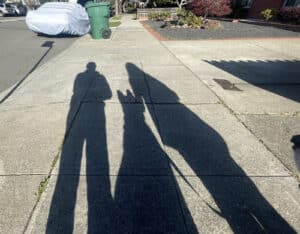 Alameda Post - shadows on the sidewalk of two humans and one dog