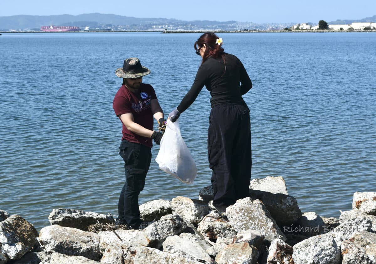 Alameda Post - one volunteer holds out a bag to another so they can put trash in it