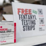 Alameda Post - a bo of Narcan next to a sign that says Free Fentanyl Testing Strips
