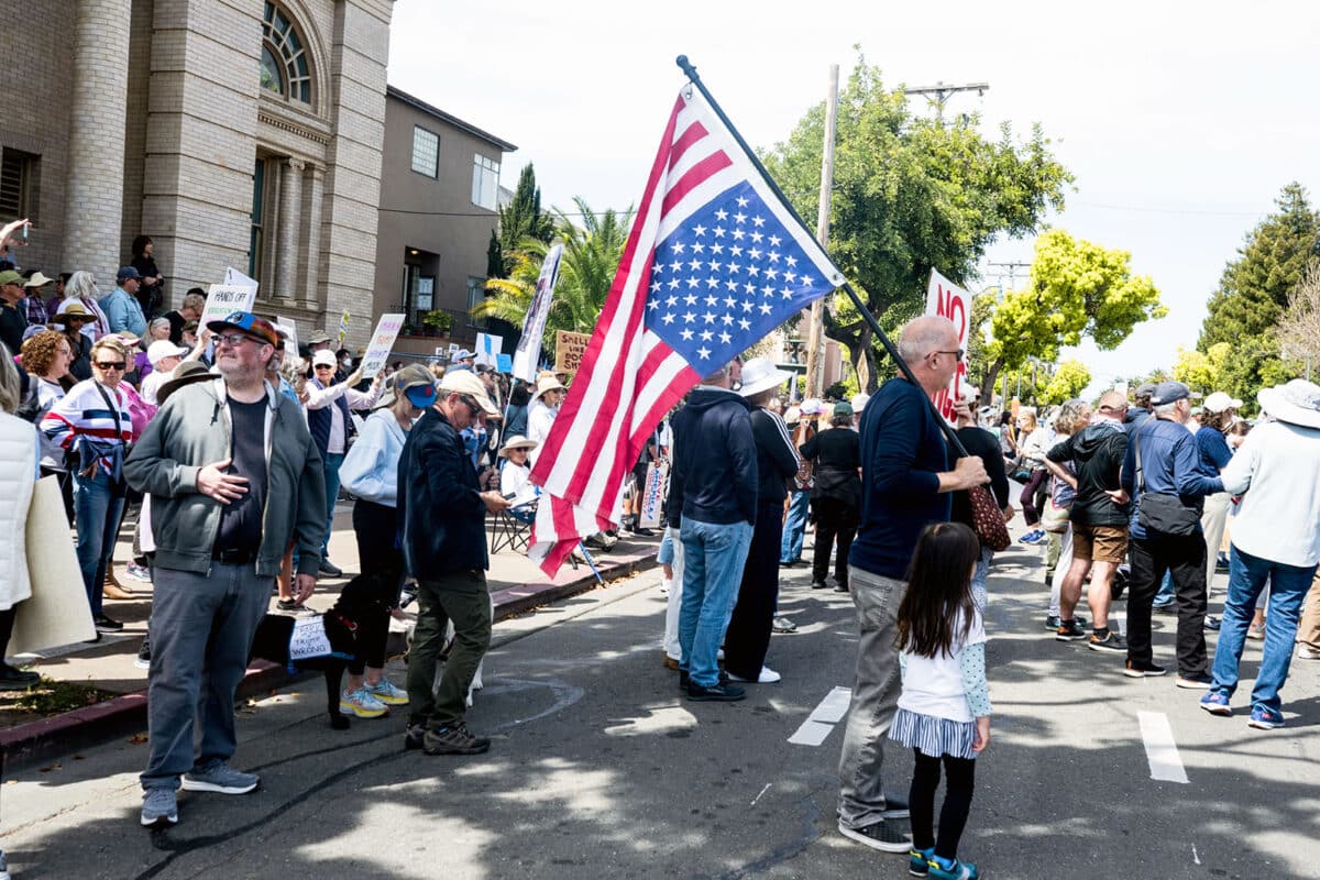 A protestor holds the American flag in the distress position at the April 5, 2025 Hands Off Rally in Alameda, CA. Photo Stephanie Penn.