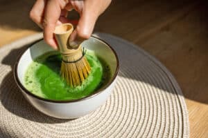 Alameda Post - A hand using a bamboo whisk to froth vibrant green matcha tea