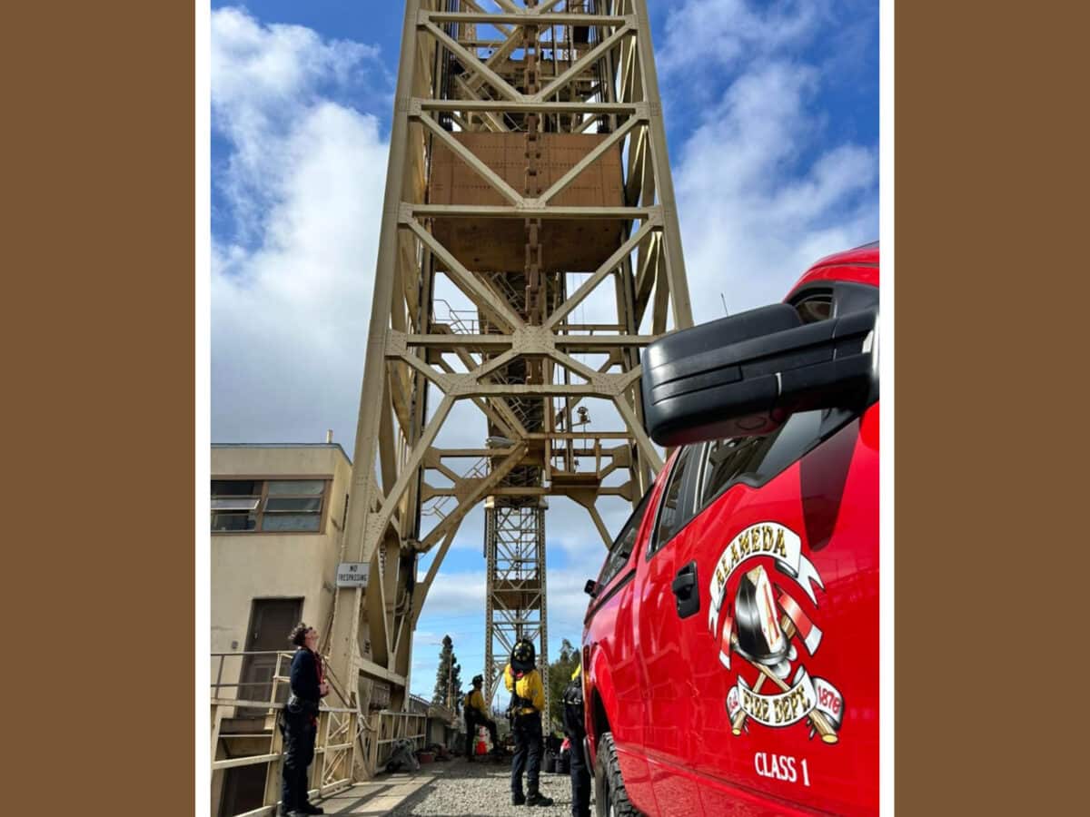 Alameda Post - an AFD vehicle and AFD firefighters are stationed near the Fruitvale bridge for rope training. They look up the tall structure.