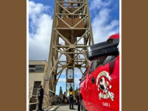 Alameda Post - an AFD vehicle and AFD firefighters are stationed near the Fruitvale bridge. They look up the tall structure.