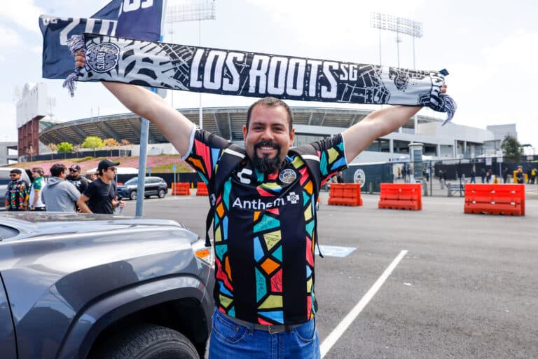 Alameda Post - an Oakland Roots fan wearing a jersey holds up a scarf that says "Los Roots" in front of the Colosseum before the match versus Orange County SC