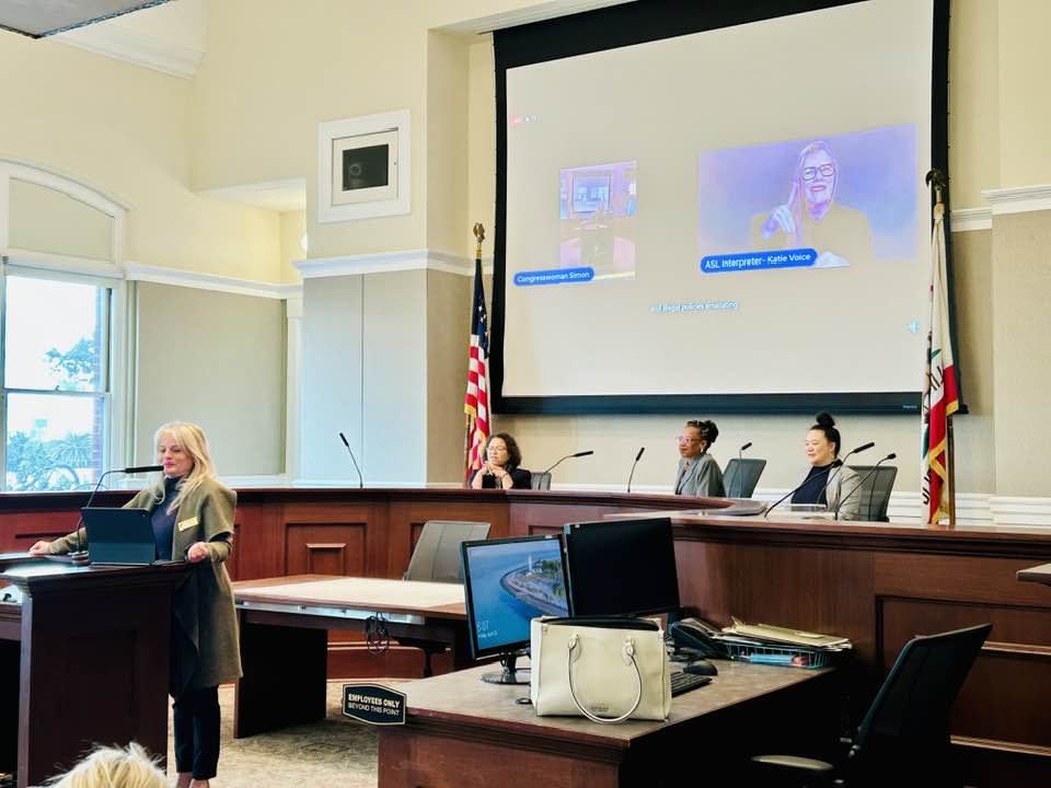 Alameda Post - at the front of City Hall Council Chamers, a woman talks into a microphone