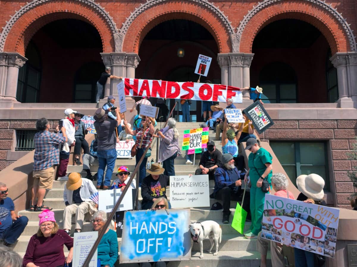 Protestors unfurl a "Hands Off" banner over Alameda City Hall during the April 5, 2025 Hands Off Rally in Alameda, CA. Photo Adam Gillitt.