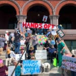 Protestors unfurl a "Hands Off" banner over Alameda City Hall during the April 5, 2025 Hands Off Rally in Alameda, CA. Photo Adam Gillitt.
