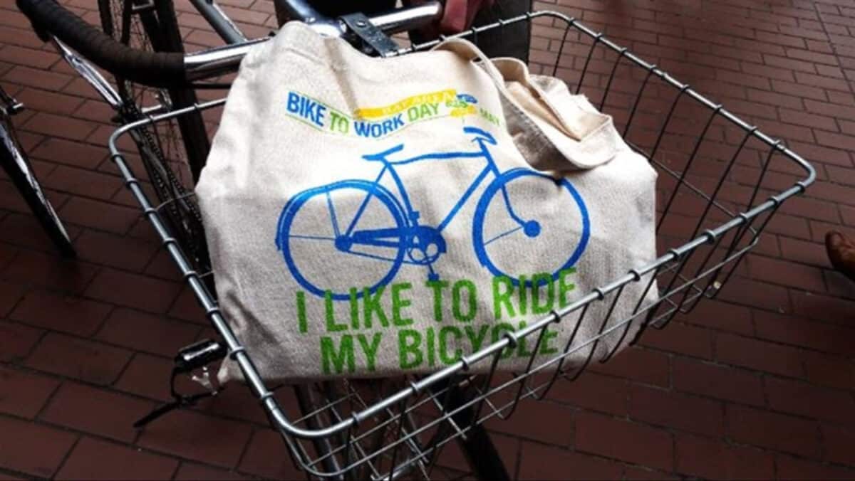 Alameda Post - a reusable canvas bag that says "Bike to Work Day. I like to ride my bicycle." sits in a bicycle basket