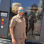 Alameda Post - Derrick Reynolds the UPS driver stands in uniform with his UPS truck and smiles