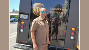 Alameda Post - Derrick Reynolds the UPS driver stands in uniform with his UPS truck and smiles