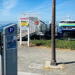 Alameda Post - a parking pay station sits at Harbor Bay Ferry Terminal. A ferry is seen out at the dock.