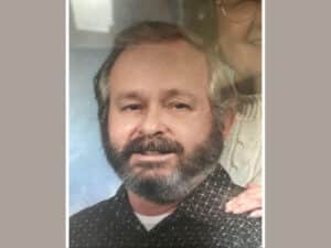 Alameda Post - James Gary Stutler smiles in a photograph. A woman that appears to be close to his age stands behind him and smiles.