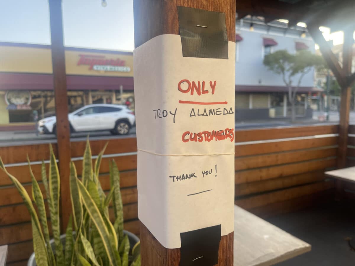 Alameda Post - a sign taped to a post an an outdoor covered eating area that says "Only Troy Alameda customers. Thank you!"