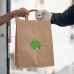 Alameda Post - a delivery driver hands food to a waiting person. Neither of their faces are visible.