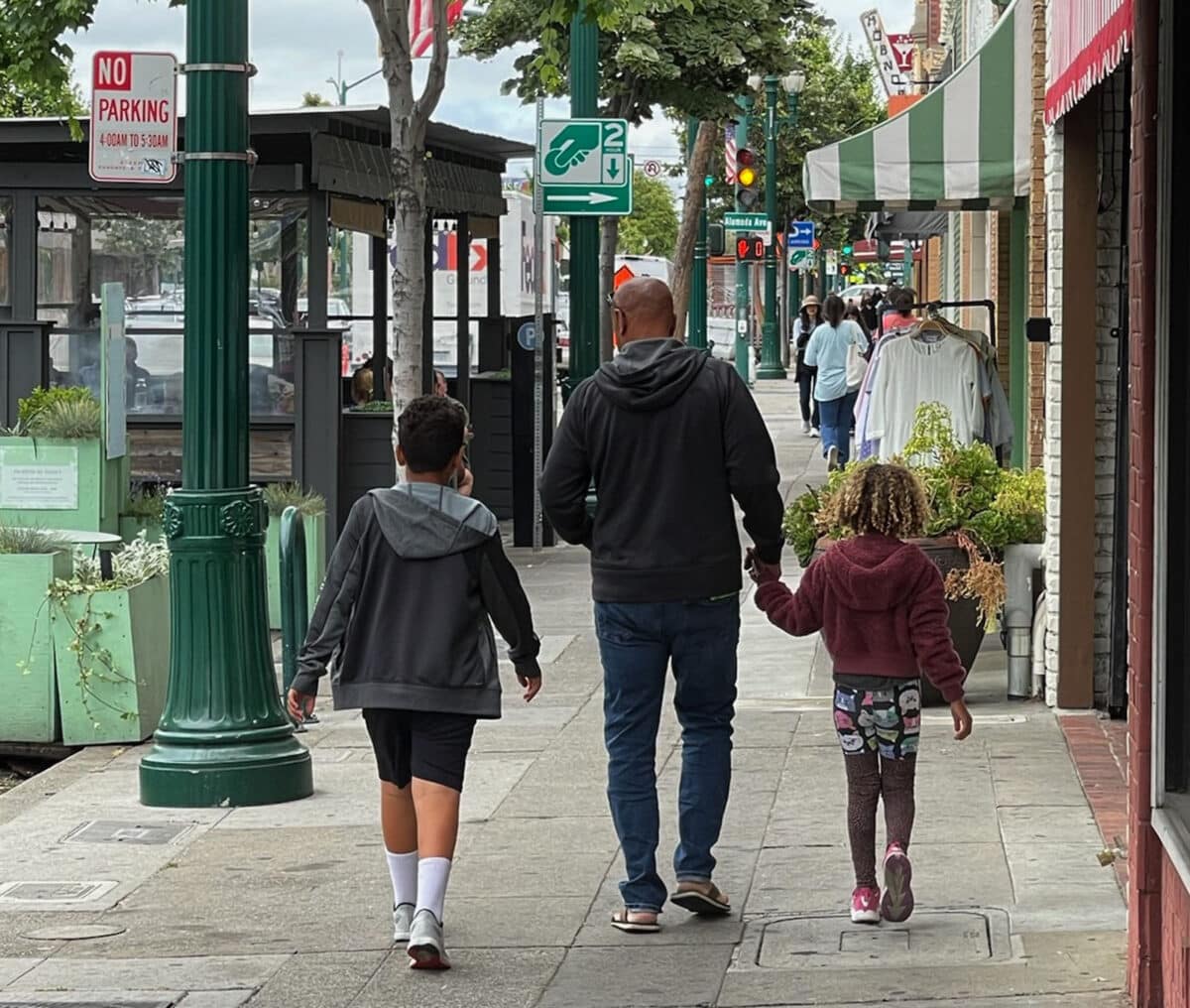 Alameda Post - a man and two children walk away from the camera down park street
