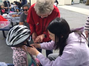 Alameda Post - adults help a young child with a helmet fitting at the Alameda Bike Festival at Paden