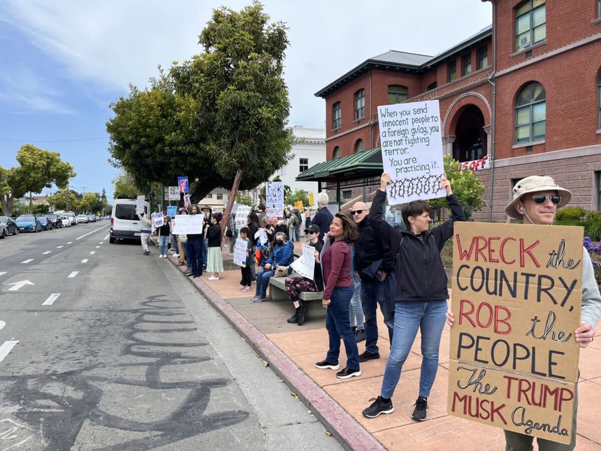 Alameda Post - protestors in front of City Hall in Alameda hold signs that say things like "Wreck the country, rob the people, the Trump Musk Agenda."