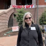 Alameda Post - a woman, Tina Davis, smiles in front of City Hall. A banner behind her says "Hands Off"
