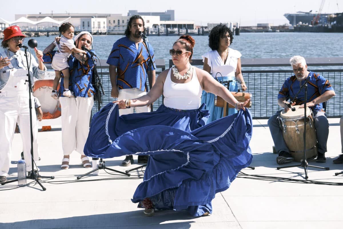 Alameda Post - a woman dances in a flowing skirt while musicians perform behind her