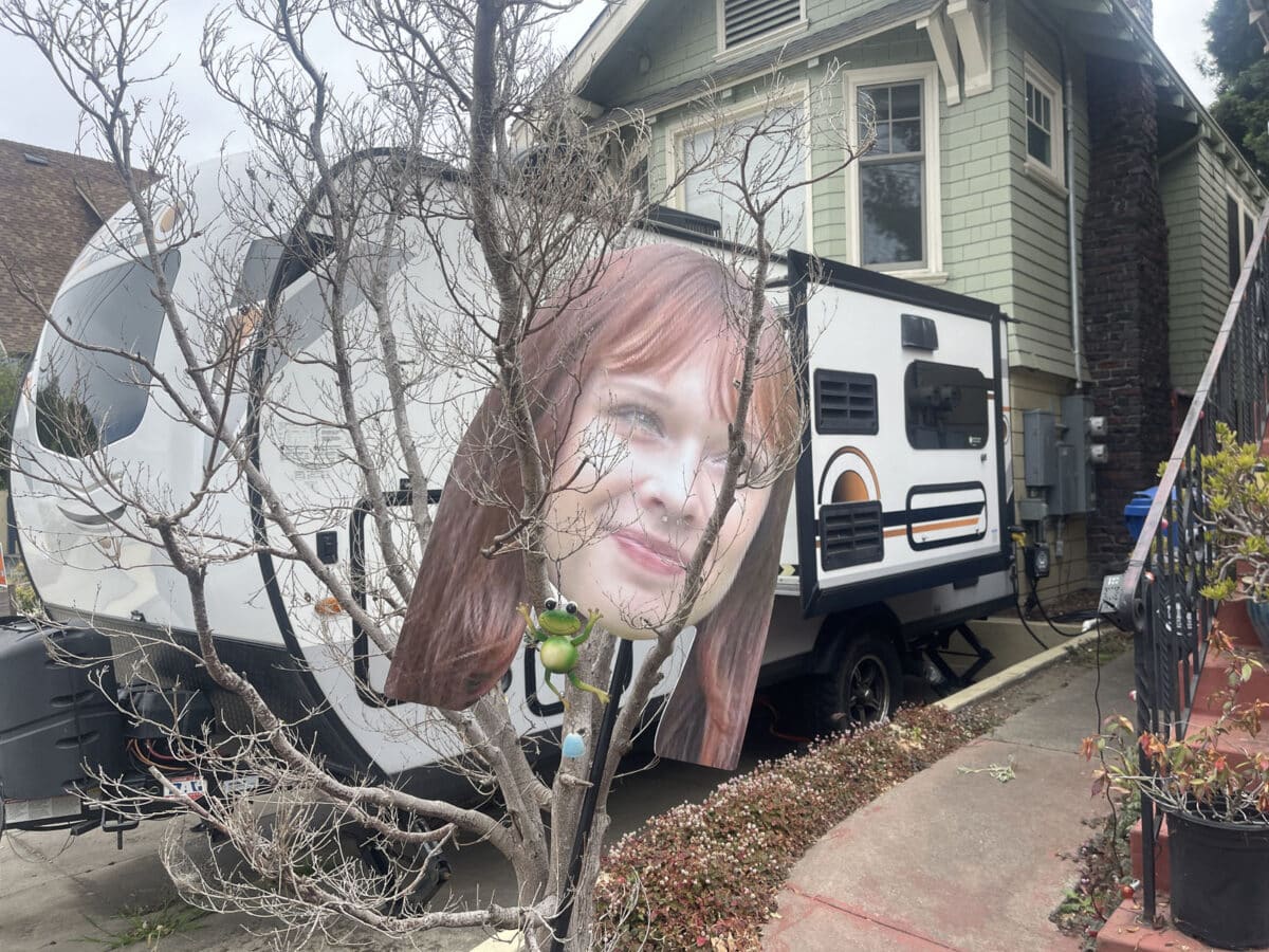 Alameda Post - a large print out, banner, or decoration of a woman's head in someone's driveway, and a toy frog