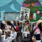 Alameda Post - participants in the Right of Return Pilgrimage gather. They look towards someone or something out of frame, raising their hands balled into fists, and holding sights that say things like "Interfaith Pilgrimage for Peace"