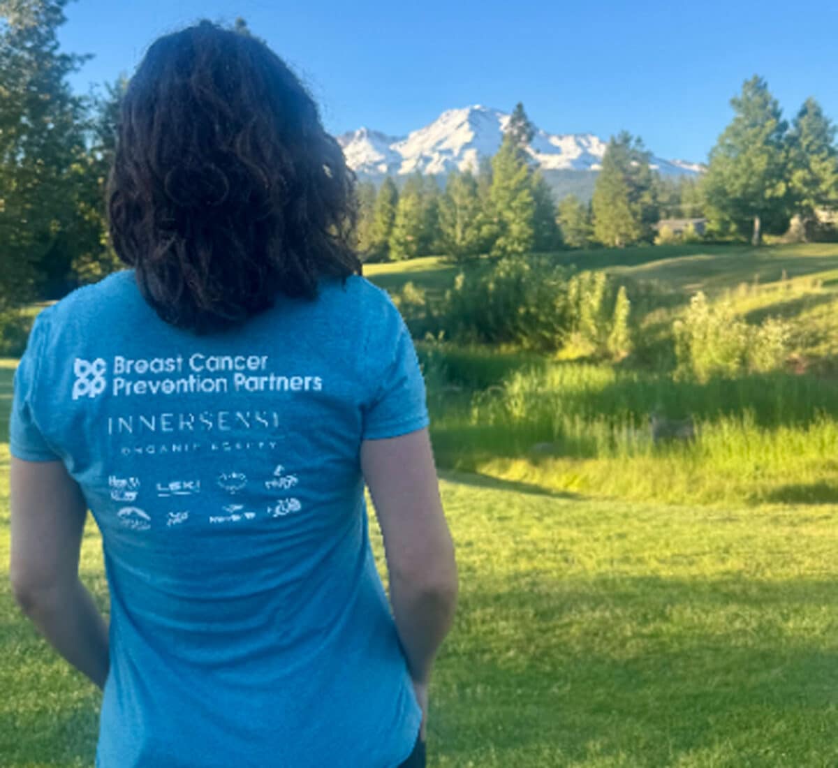 Alameda Post - a woman wears a shirt that says Breast Cancer prevention Partners and looks over a beautiful landscape