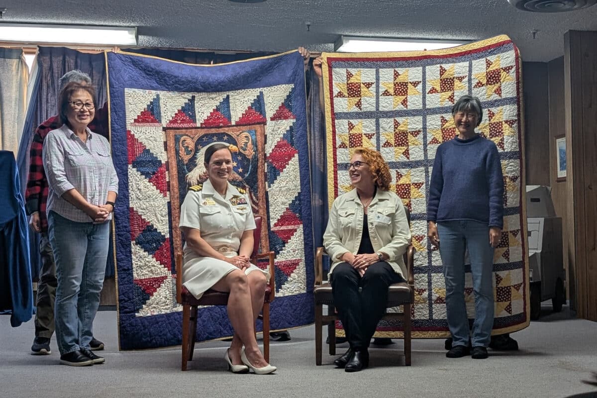 Alameda Post - Commander Trisha Kelly and Army Veteran Liz Rush sit in chairs and smile. They are in front of two beautiful quilts and besides the women who made them