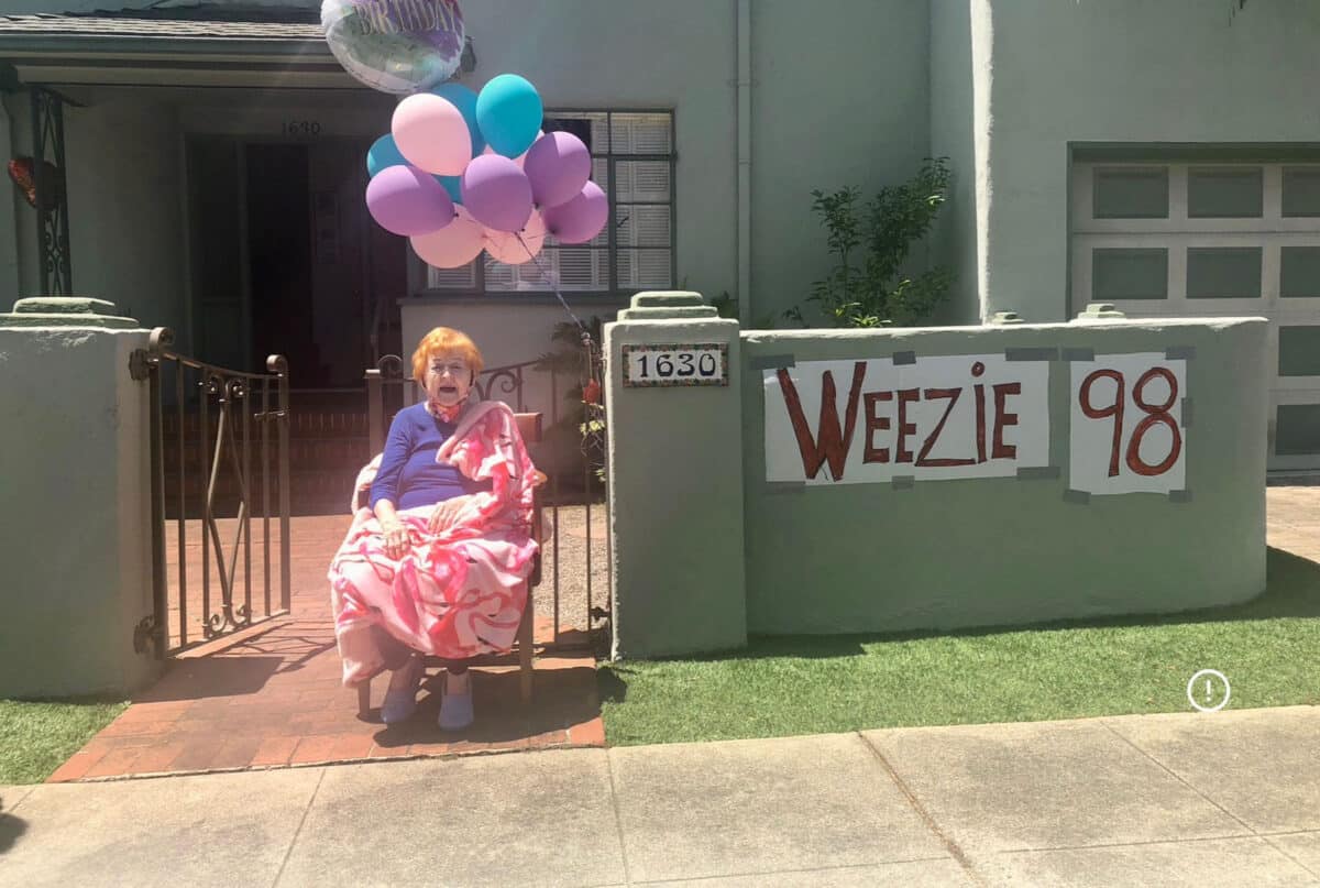 Alameda Post - Weezie Mott sits outside her home next to a large bunch of balloons. There is a banner on a front yard wall that says "Weezie 98"