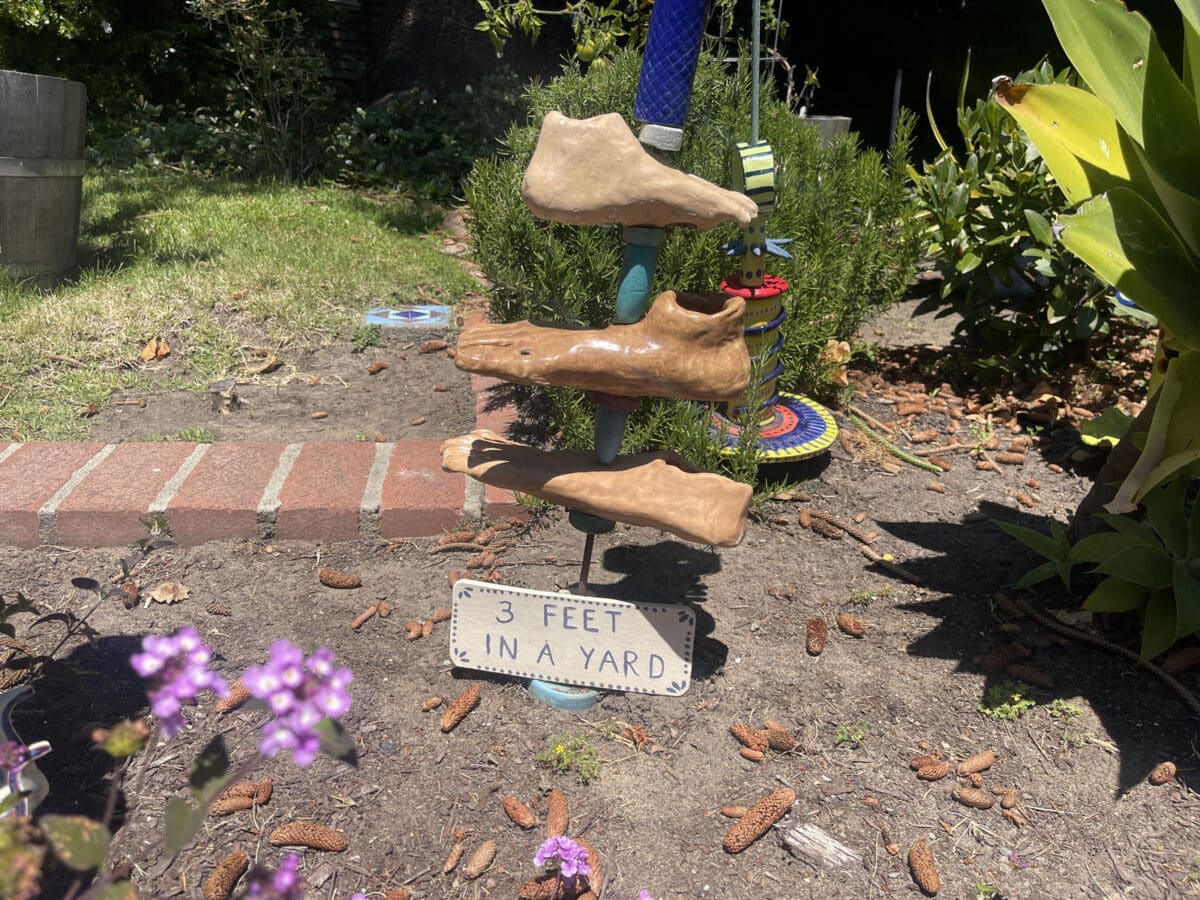 Alameda Post - a sculpture of three feet on a lawn with a sign that says "Three feet in a yard"