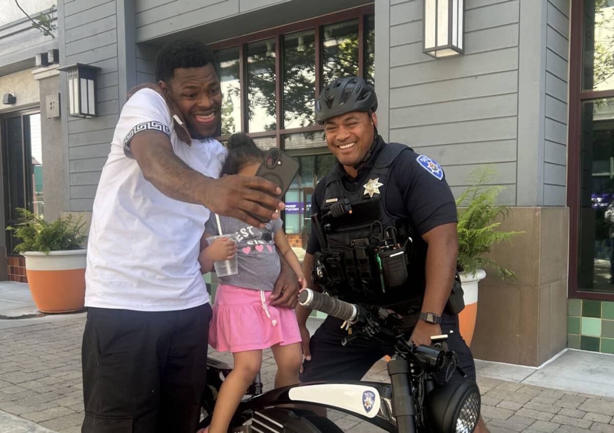 Alameda Post - a father and child take a selfie with an APD officer on a bike who is part of the new Business Patrol