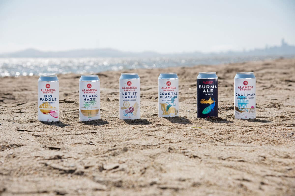 Alameda Post- six cans of beer on a beach