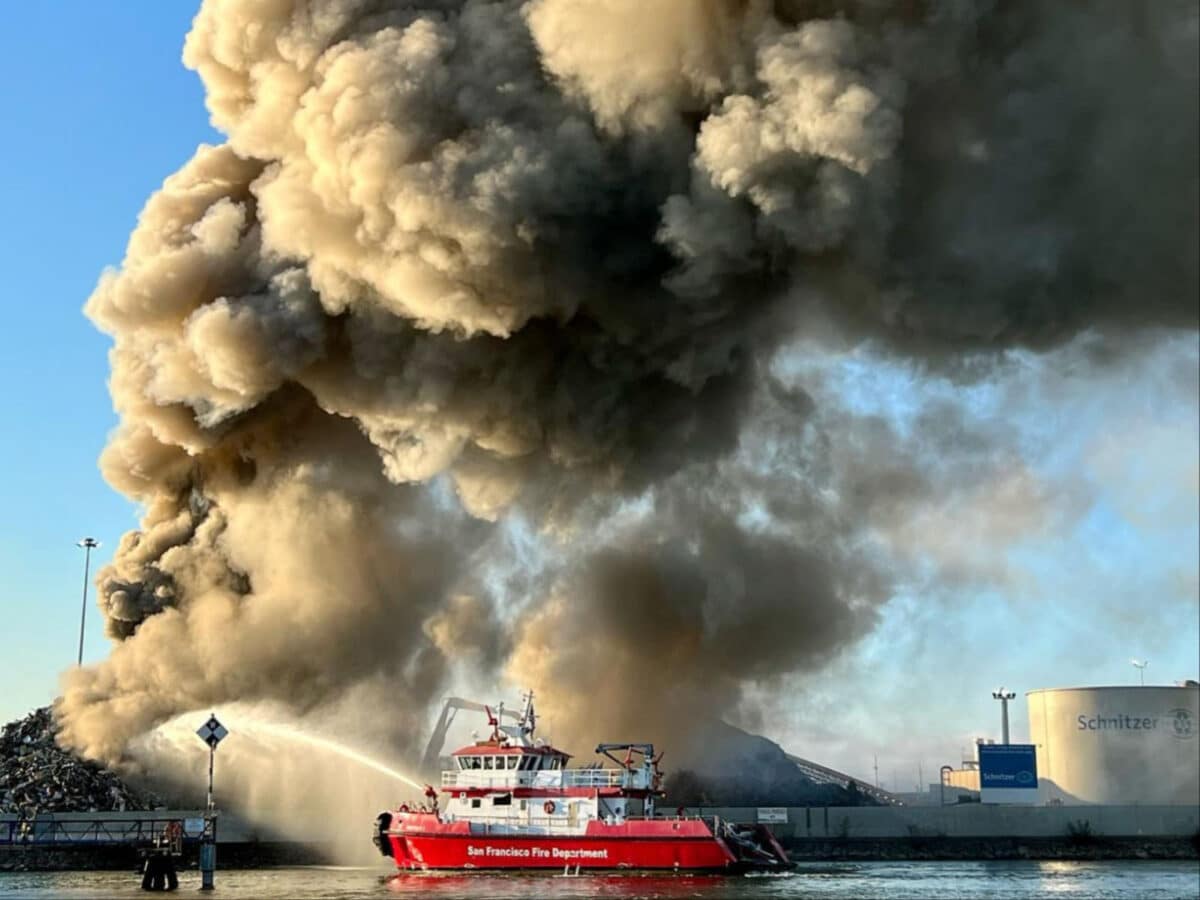 Alameda Post - a huge plume of smoke billows up from Radius Recycling and a red fire boat sprays water onto the base