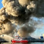 Alameda Post - a huge plume of smoke billows up from Radius Recycling and a red fire boat sprays water onto the base