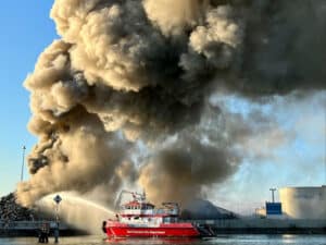 Alameda Post - a huge plume of smoke billows up from Radius Recycling and a red fire boat sprays water onto the base