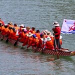 Alameda Post - the dragonflyers paddle in the water with an Alameda flag on the back of the boat