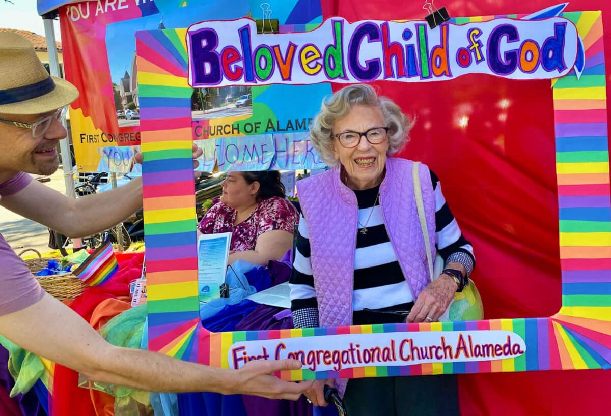 Alameda Post - Ginny Krutilek smiles inside a colorful cardboard cutout that says Beloved Child of God First Congregational Church Alameda