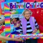 Alameda Post - Ginny Krutilek smiles inside a colorful cardboard cutout that says Beloved Child of God First Congregational Church Alameda