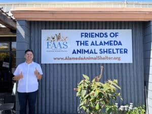 Alameda Post - Adrien Abuyen stands in front of the sign at Friends of the Alameda Animal Shelter and gives a thumbs up
